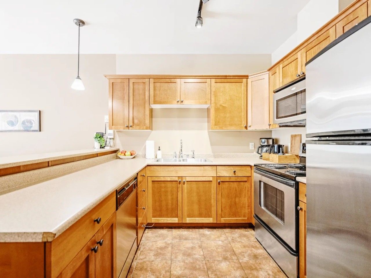 A kitchen with wooden cabinets, a stainless steel refrigerator, and a built-in oven.