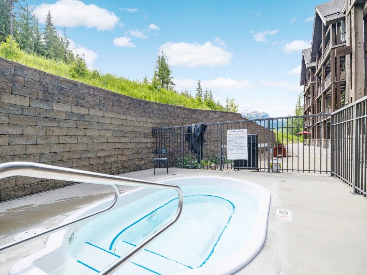 A swimming pool area with a brick wall, a metal fence, and a building with multiple balconies.