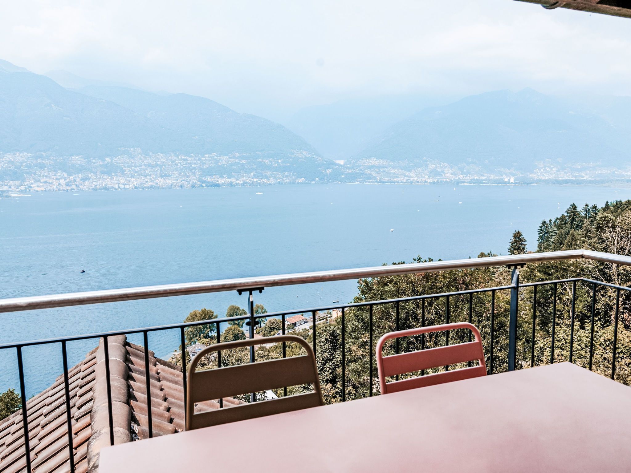 Un balcon avec une table et des chaises donnant sur une étendue d’eau et sur le panorama d’une ville lointaine.