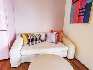 Ein gemütliches Wohnzimmer mit einer Couch, Kissen, einem kleinen runden Tisch und einem farbenfrohen abstrakten Gemälde an der Wand.