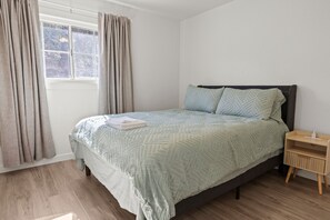 Een slaapkamer met een bed, een nachtkastje, een raam met gordijnen en uitzicht op het landschap.