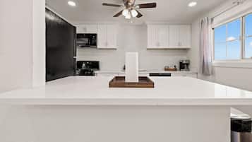 A modern kitchen with white cabinetry, a central island, and a ceiling fan.