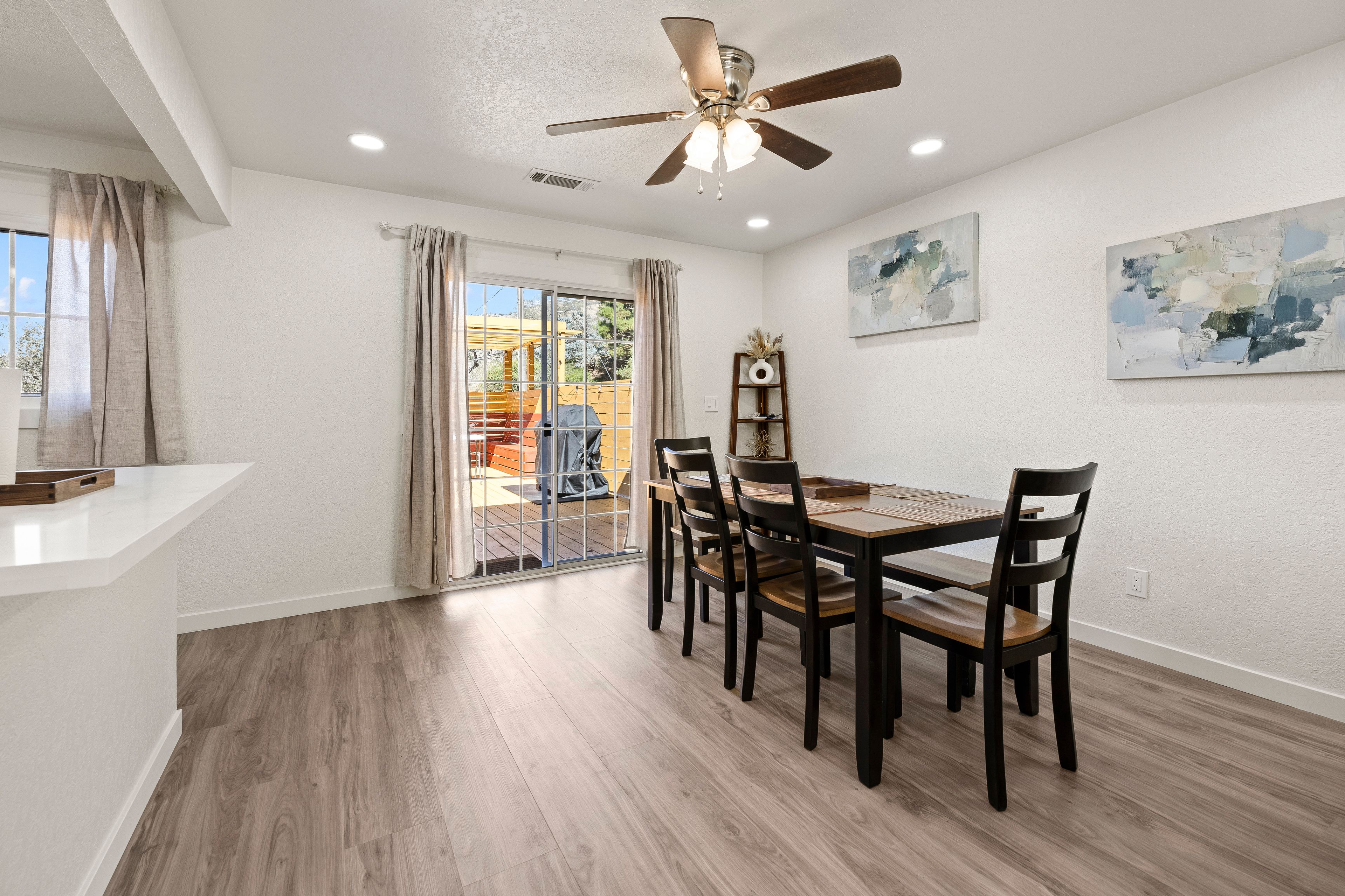 A dining area with a table and chairs, a ceiling fan, and a view through a glass door to an outdoor patio.