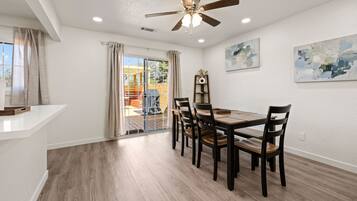 A dining area with a table and chairs, a ceiling fan, and a view through a glass door to an outdoor patio.