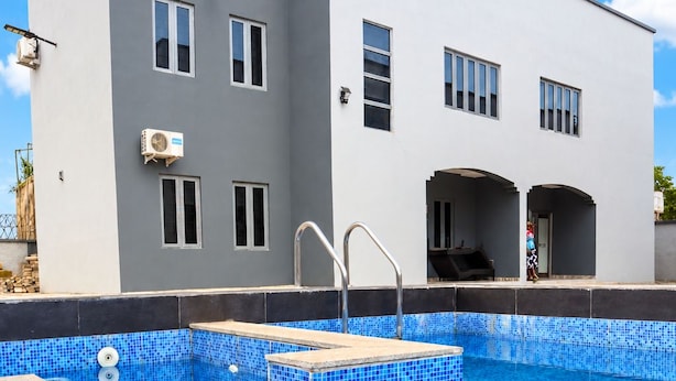 A swimming pool with blue mosaic tiles, a white building with multiple windows, and a metal ladder leading into the pool. - Xpression Apartment  (Akure)