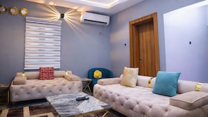 A modern living room with two sofas, a coffee table, and a window with blinds. - Xpression Apartment  (Akure)