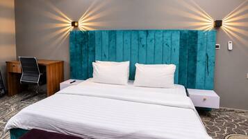 A hotel room with a bed, two bedside tables, a desk, a chair, and a wall-mounted light fixture.