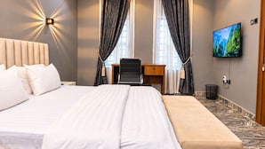 A hotel room with a large bed, a desk, a chair, a TV, and a view of mountains. - Xpression Apartment  (Akure)