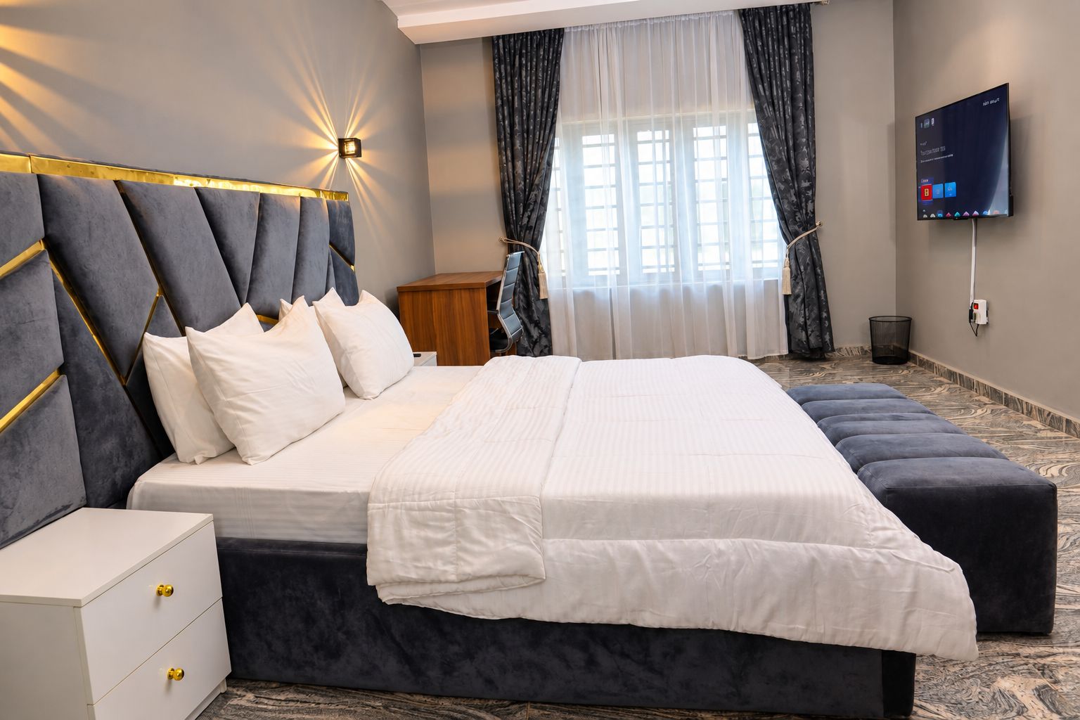 Quarto de hotel moderno com uma cama grande, mesa de cabeceira, televisão e janela com cortinas.