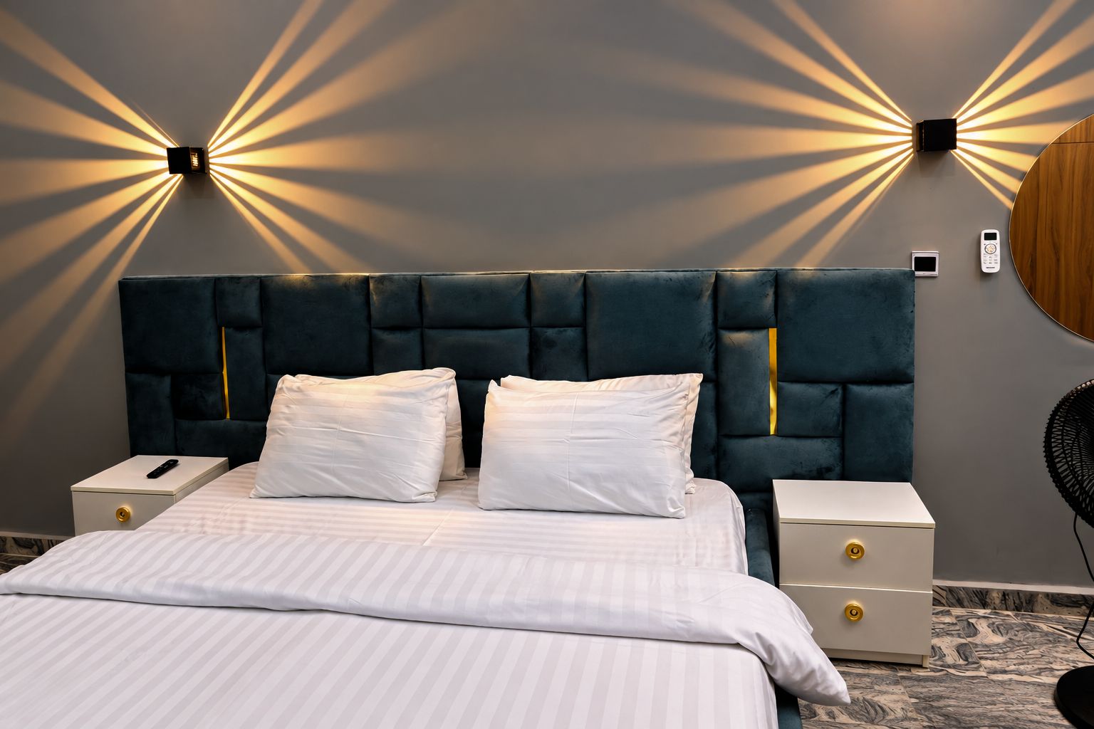 Ein modernes Schlafzimmer mit einer gesteppten Kopfteile, einem großen Bett mit weißer Bettwäsche, Nachttischen mit Schubladen und Wandleuchten.