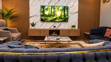 Ein modernes Wohnzimmer mit einem großen Flachbildfernseher, einem dunkelblauen Sofa, einem Marmor-Couchtisch und Holzvertäfelung an den Wänden.