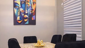 A conference room with a marble table, black chairs, a painting on the wall, and an air conditioning unit. - Xpression Apartment  (Akure)