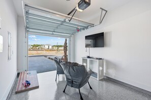 A modern room with a sliding glass door, a flat-screen TV, a grey chair, and a small table with an American flag pillow. - Salty Seahorse | New Coastal Townhome in PCB (Panama City Beach)