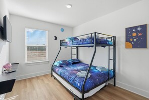 A bunk bed with a galaxy-themed bedspread, a window with blinds, a wall-mounted TV, and a space-themed wall art piece. - Salty Seahorse | New Coastal Townhome in PCB (Panama City Beach)