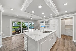 A modern kitchen with a marble island, white cabinetry, and a view of a pool area. - New! Seaside Sunset! Luxury Canal/Pool Home! 1 Mile to the Beach! (Naples)
