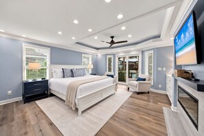 Quarto com cama, mesas de cabeceira, televisão e ventoinha no teto.