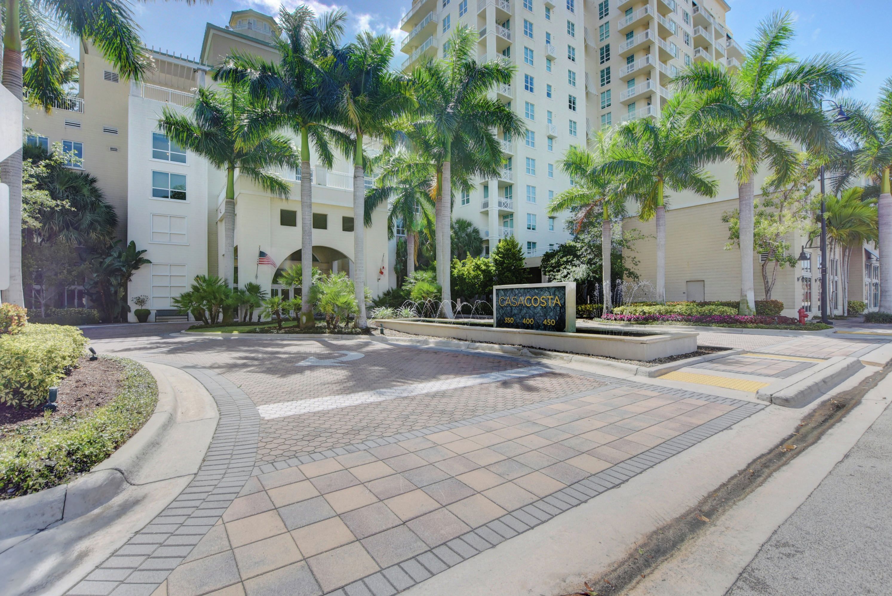 A hotel entrance with a paved walkway, palm trees, and a sign indicating the name and room numbers.
