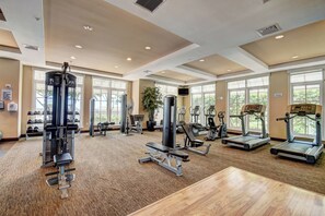 Un gimnasio espacioso con diversos equipos de ejercicio, ventanas amplias y suelo de madera.