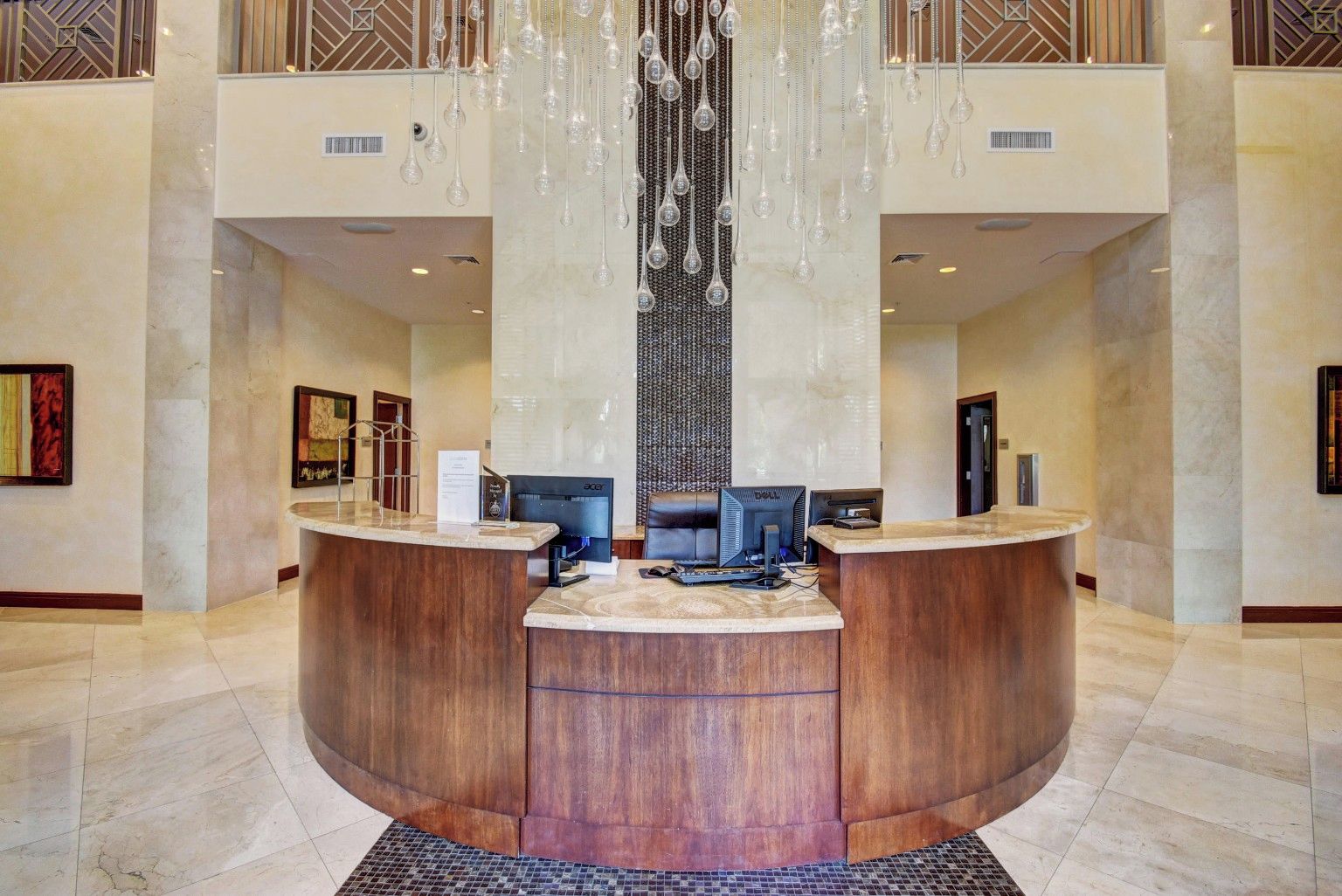 Zona de recepción de un hotel con un mostrador curvo, dos monitores de ordenador y una lámpara decorativa.