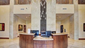 Ein Hotel-Rezeptionsbereich mit einer gebogenen Theke, zwei Computermonitoren und einer dekorativen Leuchte.