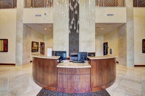 Zona de recepción de un hotel con un mostrador curvo, dos monitores de ordenador y una lámpara decorativa.