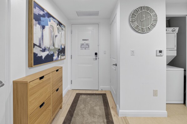 Un couloir avec une armoire en bois, un tableau, une horloge et une porte sur laquelle est apposé un panneau « Il est interdit de fumer ».