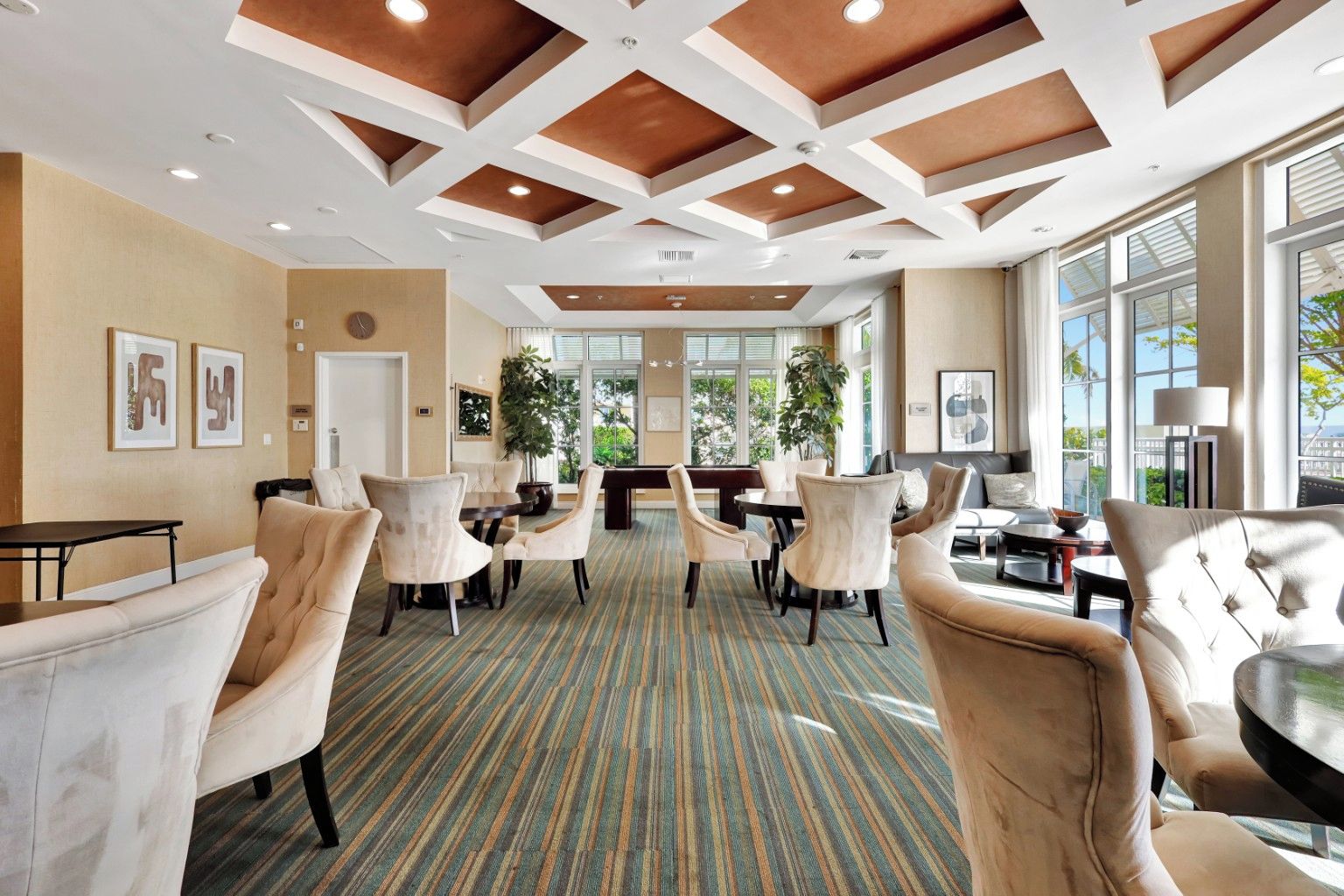 A hotel lobby with a central seating area, multiple chairs, a pool table, and large windows providing natural light.