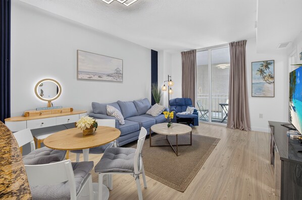 A modern living room with a blue sofa, a round wooden coffee table, and a dining area with a white table and chairs.