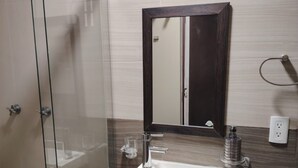 A bathroom with a glass shower enclosure, a sink with a mirror above it, and a dark wooden cabinet. - Cozy Urban Apartment (Coxcatlán)