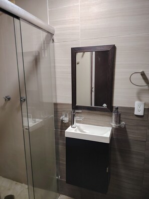A bathroom with a glass shower enclosure, a sink with a mirror above it, and a dark wooden cabinet.