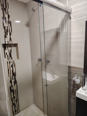 A modern bathroom with a glass-enclosed shower, a sink with a glass container, and a decorative wall panel.