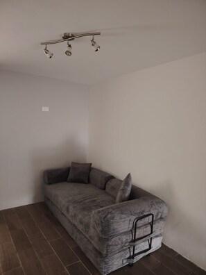 A corner room with a grey sofa, a ceiling light fixture, and a power outlet on the wall.