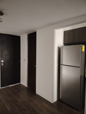 A hallway with a dark wooden floor, white walls, and a stainless steel refrigerator. - Cozy Urban Apartment (Coxcatlán)
