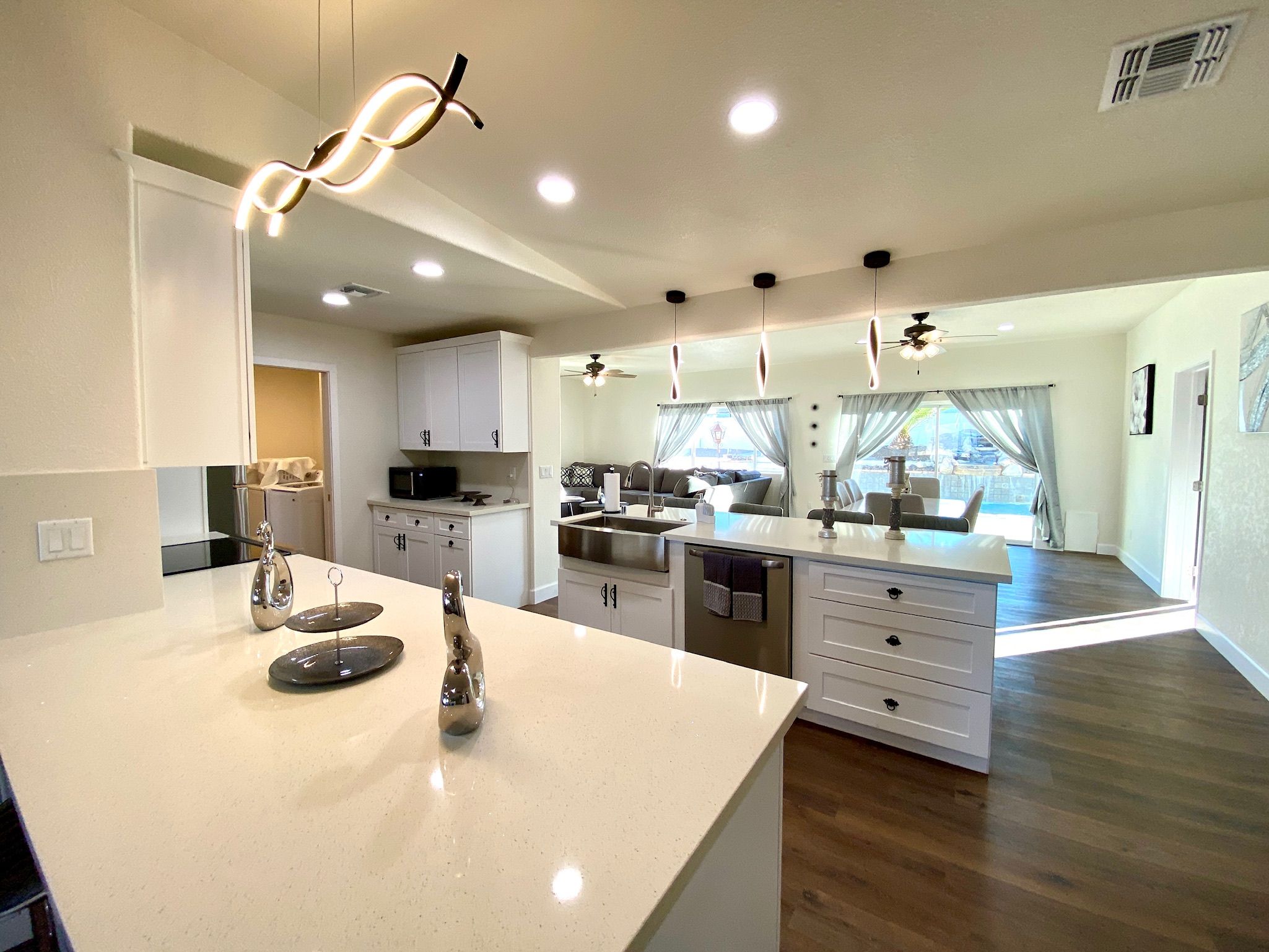 Una cocina moderna con una isla central, luces colgantes y vistas a un comedor.