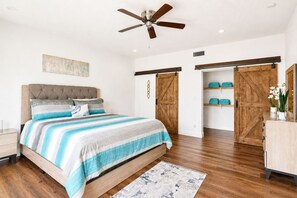 Quarto com cama, ventoinha no teto, assoalho de madeira e uma janela grande.
