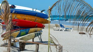 Een strand met surfplanken gestapeld op een houten bankje en een palmboom op de voorgrond.