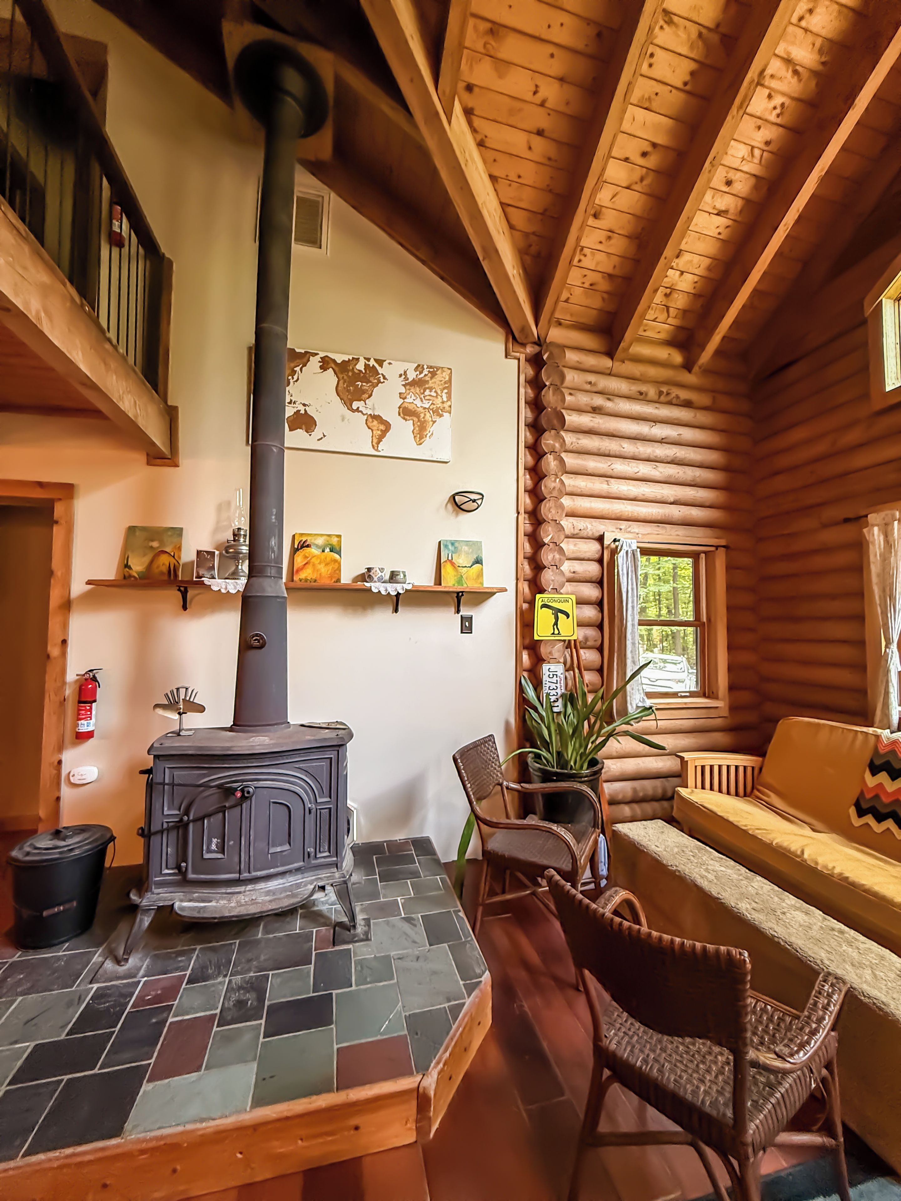 L'intérieur d'un chalet confortable, avec des murs en rondins de bois, un poêle à bois au centre, une carte accrochée au mur et un coin salon accueillant.