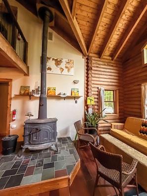 A cozy log cabin interior with a central wood-burning stove, a map on the wall, and a comfortable seating area. - A Cozy Four Bedroom Log Home in the Heart of the Catskills (Saugerties)