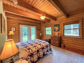 A log cabin bedroom with a bed, two windows, a dresser, and a lamp. - A Cozy Four Bedroom Log Home in the Heart of the Catskills (Saugerties)