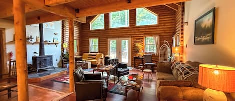 L’intérieur d’une cabane en rondins, avec une cheminée, plusieurs coins salon et de grandes fenêtres.