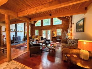 A log cabin interior with a fireplace, multiple seating areas, and large windows. - A Cozy Four Bedroom Log Home in the Heart of the Catskills (Saugerties)