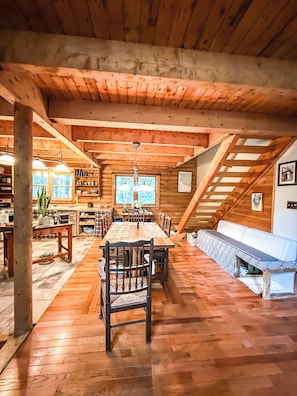 A spacious dining area with a long wooden table, chairs, and a high ceiling with wooden beams.