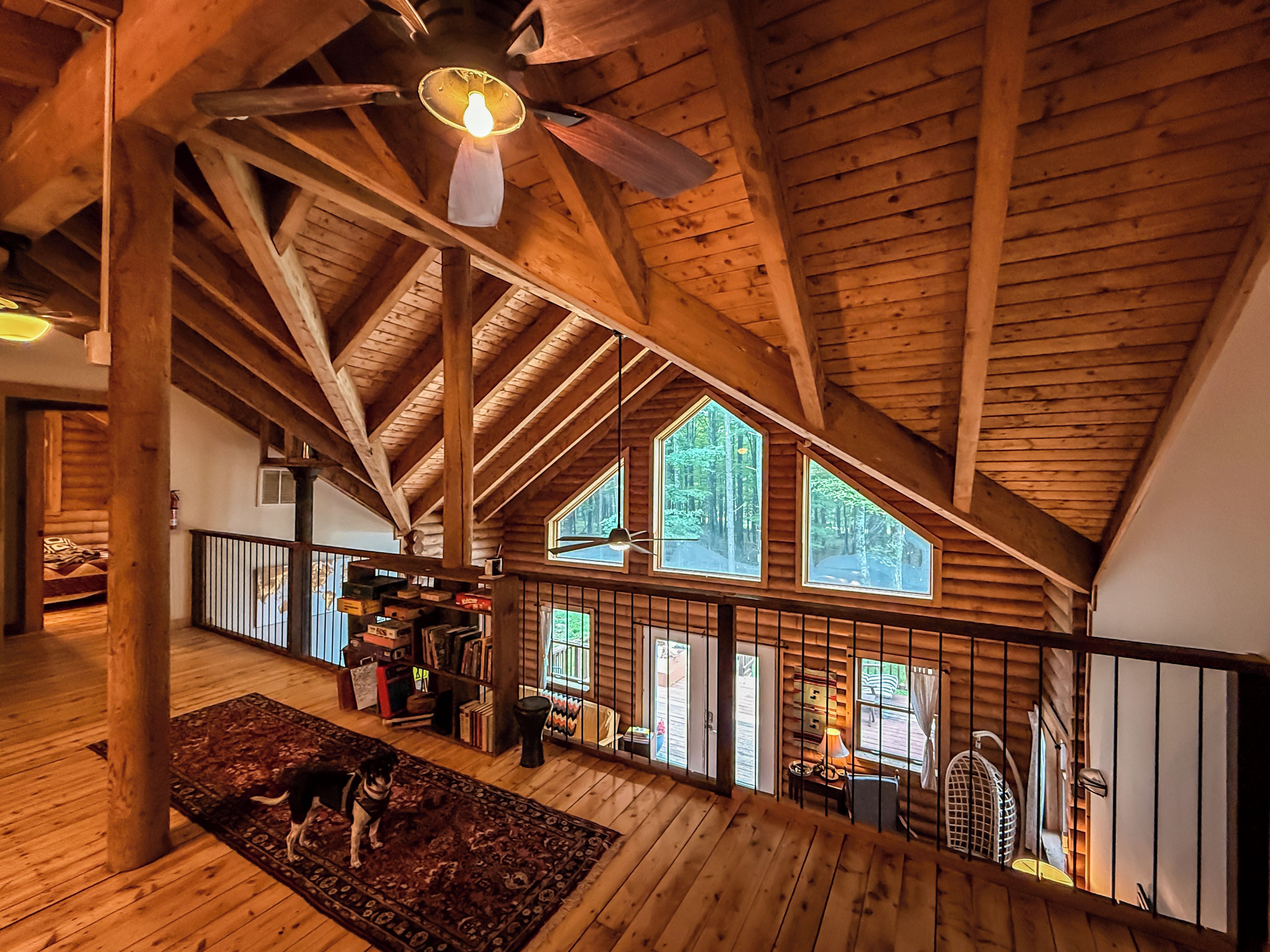 A spacious loft with high ceilings, wooden beams, and large windows offering views of the outdoors.