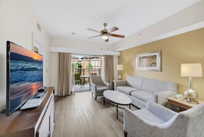 A hotel room with a television, seating area, ceiling fan, and a view through the glass door. - 2BR Disney Condo | FREE Resort Access & Parking (Orlando)