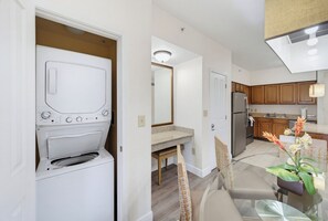 A compact kitchen with wooden cabinets, a refrigerator, and a dining area with a table and chairs. - 2BR Disney Condo | FREE Resort Access & Parking (Orlando)