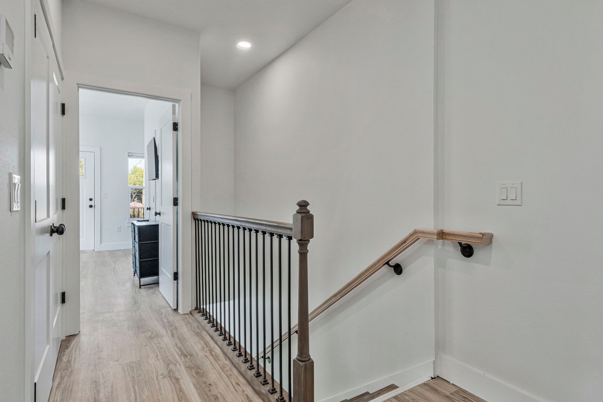 A hallway with a wooden staircase, white walls, and a door leading to a kitchen area.