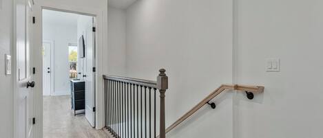 A hallway with a wooden staircase, white walls, and a door leading to a kitchen area.