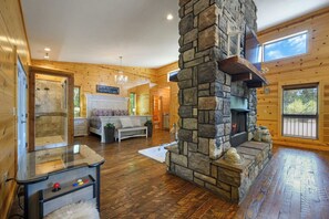 A log cabin interior with a stone fireplace, a glass-top coffee table, and a chandelier. - Song of Songs - Private Hot Tub (Broken Bow)
