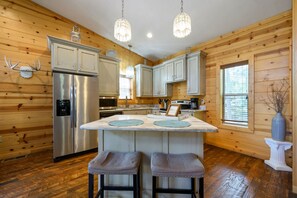 A cabin-style kitchen with wooden walls, a central island, stainless steel appliances, and pendant lighting. - Song of Songs - Private Hot Tub (Broken Bow)