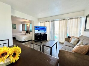 A hotel room with a bed, a TV, a sofa, a dining table, and a window with curtains. - FREE PARKING!! 2 Bedroom Vacation Rental - Corner Unit with Great Views! (Honolulu)
